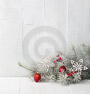 Fir branch with Christmas decorations on white rustic wooden background.