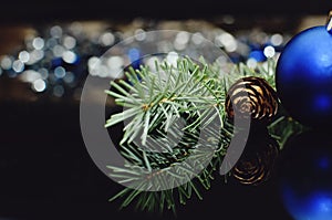 Fir branch with a pine cone and New Year`s decorations on a black background with bokeh. Beautiful Christmas background