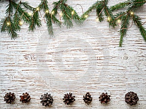 Fir branches; cone; New Year`s garland; glowing lights on old shabby wooden background.