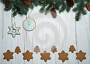 Fir branches and cones, gingerbread in the form of stars, Christmas trees, snowflakes and clocks on a light wooden background.Chri