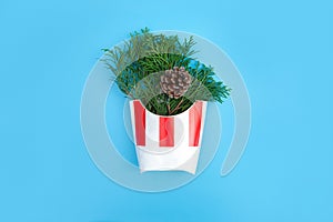 Fir branches and cones in a white and red french fries paper box on blue background. Christmas and New year concept. Front view