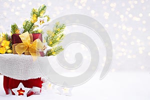 Fir branches, gift box with bow and star bulbs with defocused lights in bag on snow. Christmas, New Year