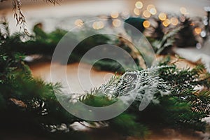 Fir branches, pine cones closeup  and golden lights glowing on wooden table. Rustic Christmas wreath workshop. Authentic stylish