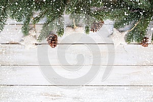 Fir leaves and pine cones decorating rustic elements on white wood table with snowflake