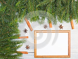 Fir tree branch with anise, cinnamon, snowflake, frame on white wooden background