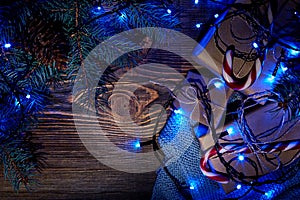 Fir tree branch with christmas lights, gift box and candy canes on wooden background with copy space.