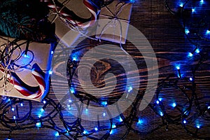 Fir tree branch with christmas lights, gift box and candy canes on wooden background with copy space.