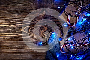 Fir tree branch with christmas lights, gift box and candy canes on wooden background with copy space.