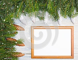 Fir tree branch with cones, frame, snowflake on white wooden background