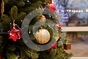 Fir tree branches decorated for Merry Christmas with red and golden ornaments, garland. Lights bokeh behind window, street