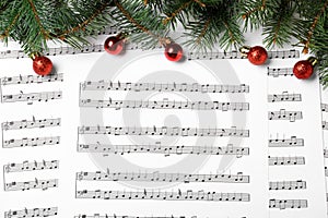 Fir tree branches and red balls on Christmas music sheets with notes, flat lay