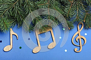 Fir tree branches with wooden music notes on blue background, flat lay. Christmas celebration