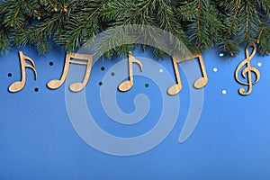 Fir tree branches with wooden music notes and space for text on blue background, flat lay. Christmas celebration