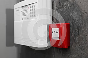 Fire alarm push button and house security system control panel on grey wall