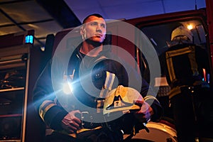 The fire brigade came to the call at night. Handsome fireman wearing a protective uniform with a flashlight included