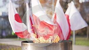 A fire burns in a candle during a national holiday against a backdrop of flying Polish flags.