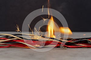 fire burns in twisted electric wires, sparks fly on a dark background. A short circuit in the electrical wiring,