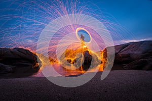 Fire dancer swing fire dancing show on the beach with dark clouds, twilight sky background.