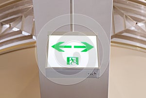 Fire exit green emergency exit signs ceiling is background. Warning plate with running man icon and arrow to left, right way.
