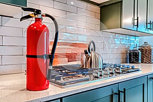 Fire extinguisher and cooktop with kettle on the countertop inside home kitchen