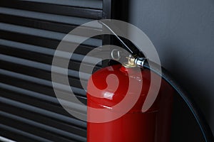 Fire extinguisher near grey wall indoors, closeup. Space for text