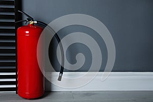 Fire extinguisher near grey wall. Space for text
