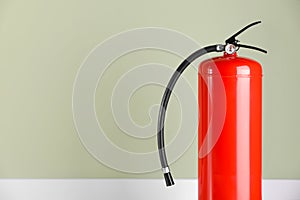 Fire extinguisher near pale green wall, space for text