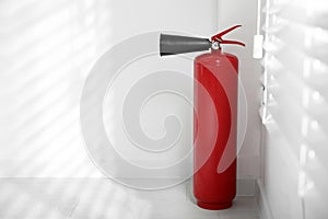 Fire extinguisher near white wall. Space for text