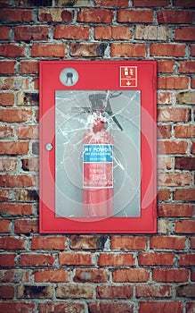 Fire extinguisher in wall box with cracked glass. brick wall