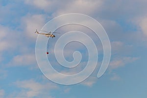 A fire fighter helicopter with a full basket of water flies against a beautiful sky