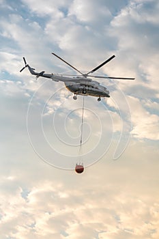 A fire fighter helicopter with a full basket of water flies against a beautiful sky