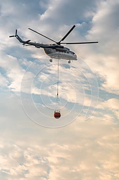 A fire fighter helicopter with a full basket of water flies against a beautiful sky