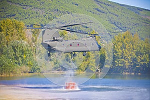 Fire fighting helicopter of the Italian army flying over a lake to collects water in a bucket to extinguish a fire