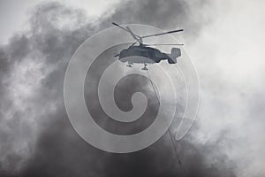 Fire fighting helicopter silhouette with bambi bucket for Ñarrying water to put out a massive building city fire, process of put