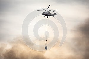 Fire fighting helicopter silhouette with bambi bucket for Ñarrying water to put out a massive building city fire, process of put