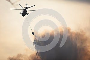 Fire fighting helicopter silhouette with bambi bucket for Ñarrying water to put out a massive building city fire, process of put