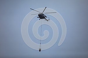 Fire fighting helicopter silhouette with bambi bucket for Ñarrying water to put out a massive building city fire, process of put