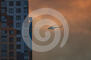 Fire fighting helicopter silhouette with bambi bucket for Ñarrying water to put out a massive building city fire, process of put