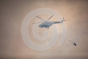 Fire fighting helicopter silhouette with bambi bucket for Ñarrying water to put out a massive building city fire, process of put