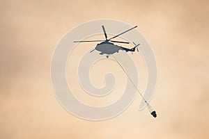 Fire fighting helicopter silhouette with bambi bucket for Ñarrying water to put out a massive building city fire, process of put