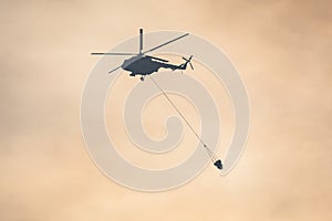 Fire fighting helicopter silhouette with bambi bucket for Ñarrying water to put out a massive building city fire, process of put
