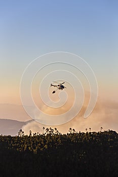 Fire-fighting helicopter with a water bucket fighting a fire on