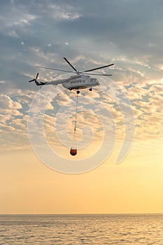 A fire helicopter collects water into the sea and flies toward the mountains to extinguish a forest fire on the