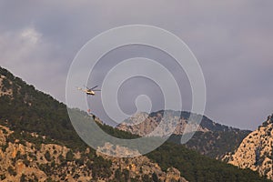 A fire helicopter with a full basket of water flies to extinguish a forest fire against the backdrop of mountains