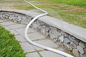 Fire hose along walkway, over fence, on meadow.