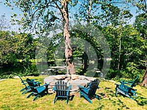 A fire pit under a tree surrounded by few wooden chairs