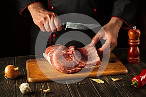 For a fire, raw ribs must be cut into small pieces. Hands of a chef with a knife in the kitchen. Cooking delicious food for a