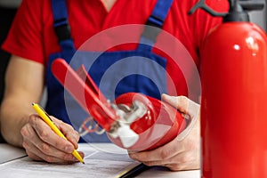 Fire safety equipment control - service engineer checking extinguisher condition and writing documents