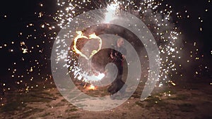 Fire show man artist twist fire objects in his hands with burning heart on background