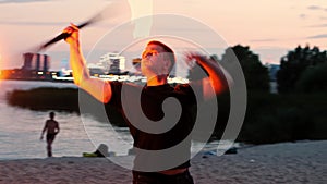 Fire show - a man in black clothes dancing with a torch in his hands on the beach at late evening